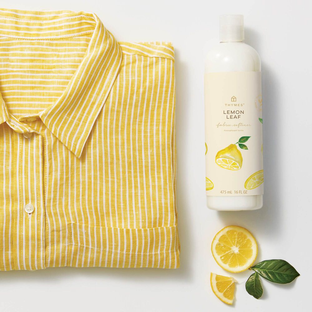 Thymes Lemon Leaf Fabric Softener to Soften Clothing with Citrus Scent next to yellow shirt and lemon slices image number 1